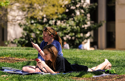 Two students on lawn looking at their iPhones